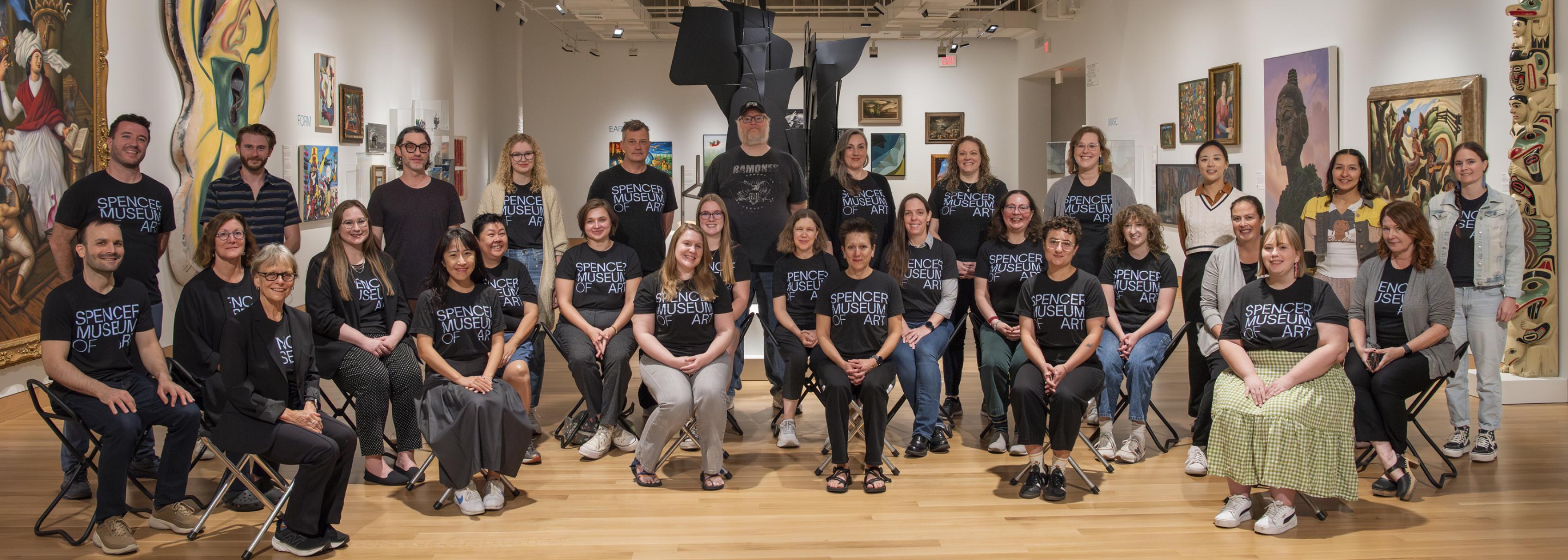 A group of people wearing matching black shirts that read 'Spencer Museum of Art' are seen in a museum gallery