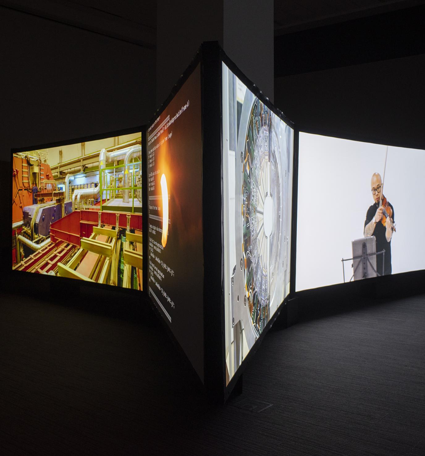 Four large screens in a dark room, each show a different image; two face left and two face right