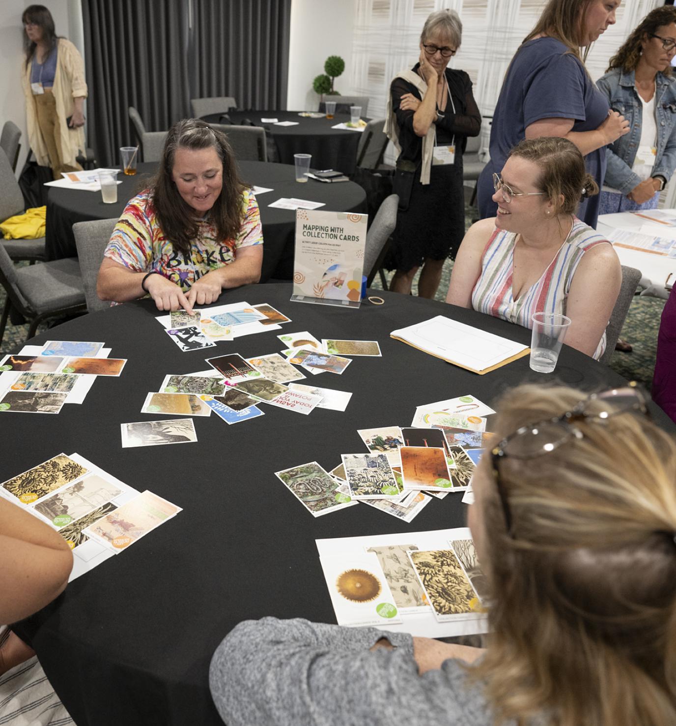 A group of white women sit around a table with brightly colored cards laid out in front of them