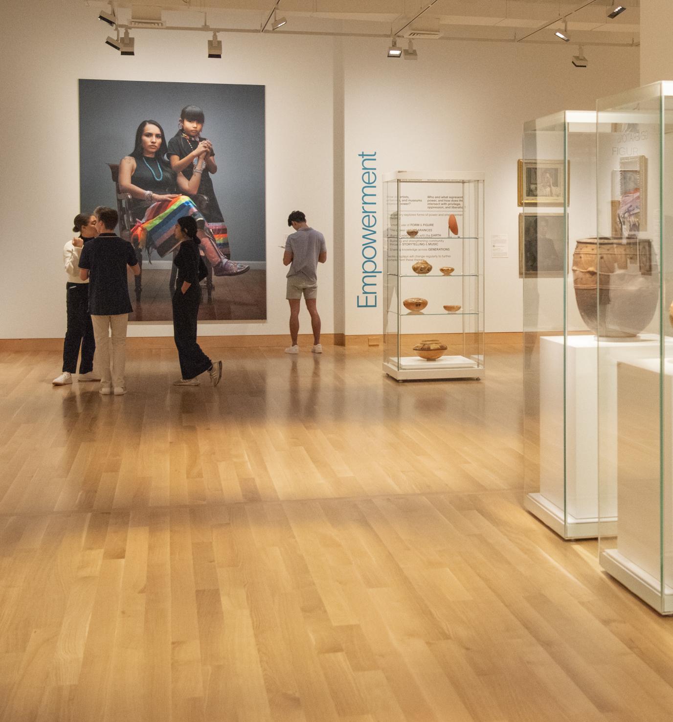 Photo of adults standing in an art gallery; pottery in glass cases lines the wall in the foreground