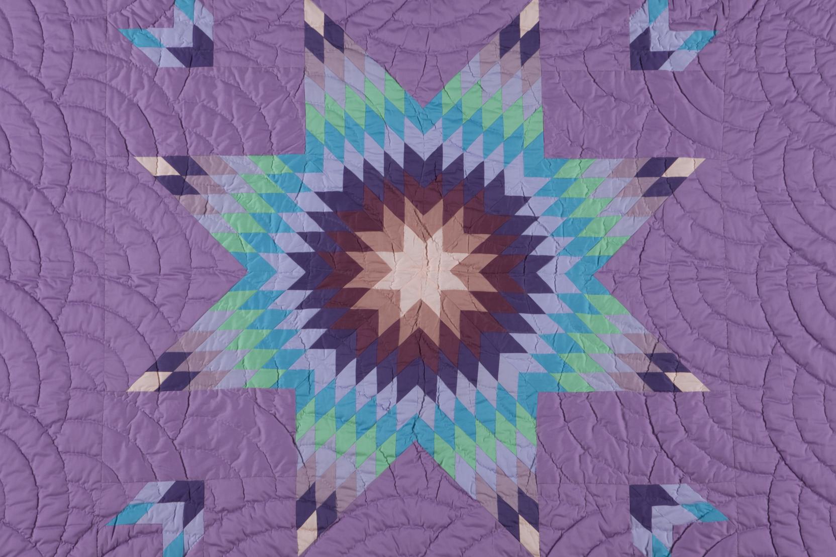 Purple quilt with a large 8-point star that radiates out from the center in different shades of purple, blue, and green 