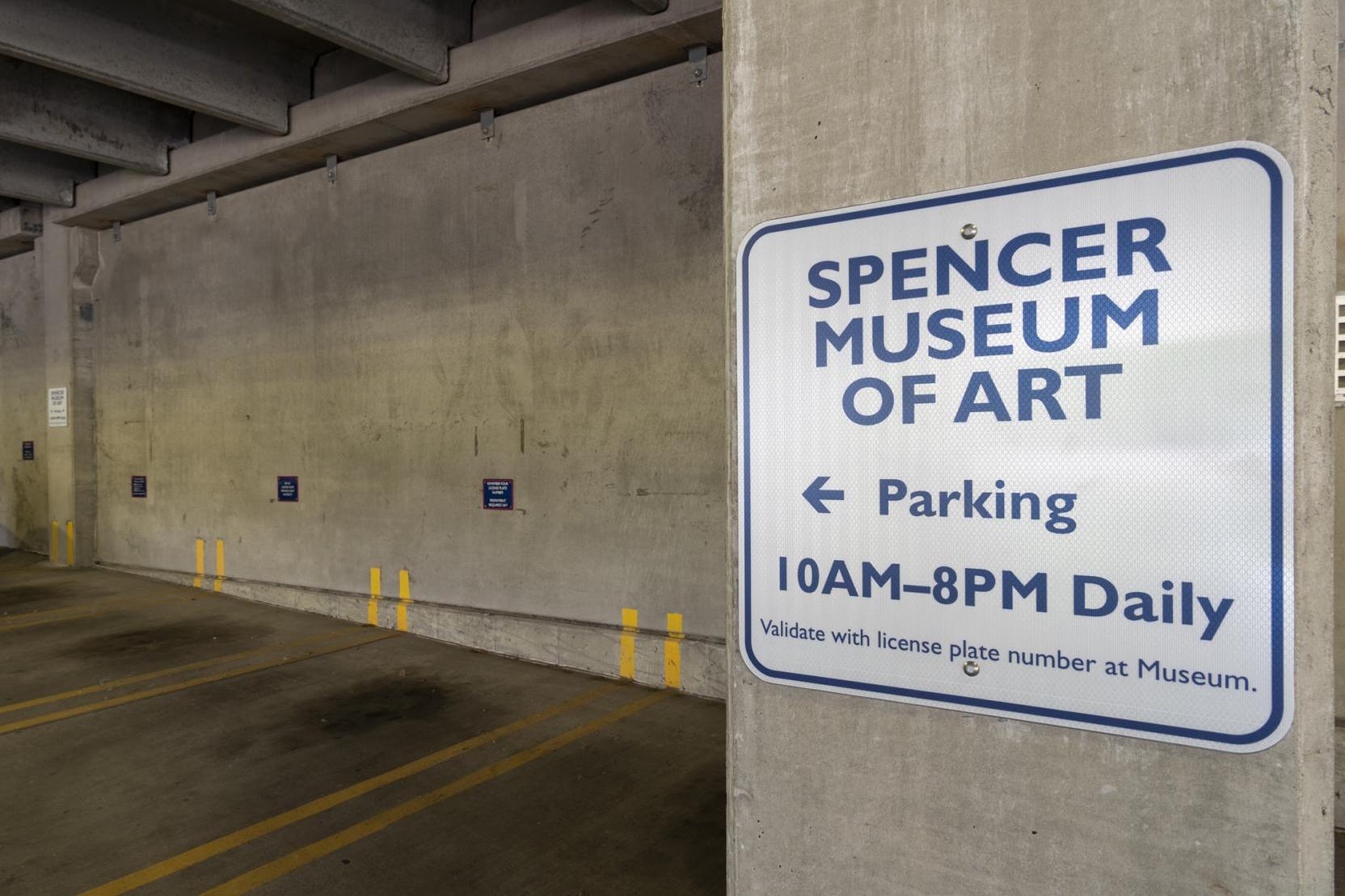 Photograph of a sign in a parking garage that reads “Spencer Museum of Art Parking, 10AM-8PM daily”