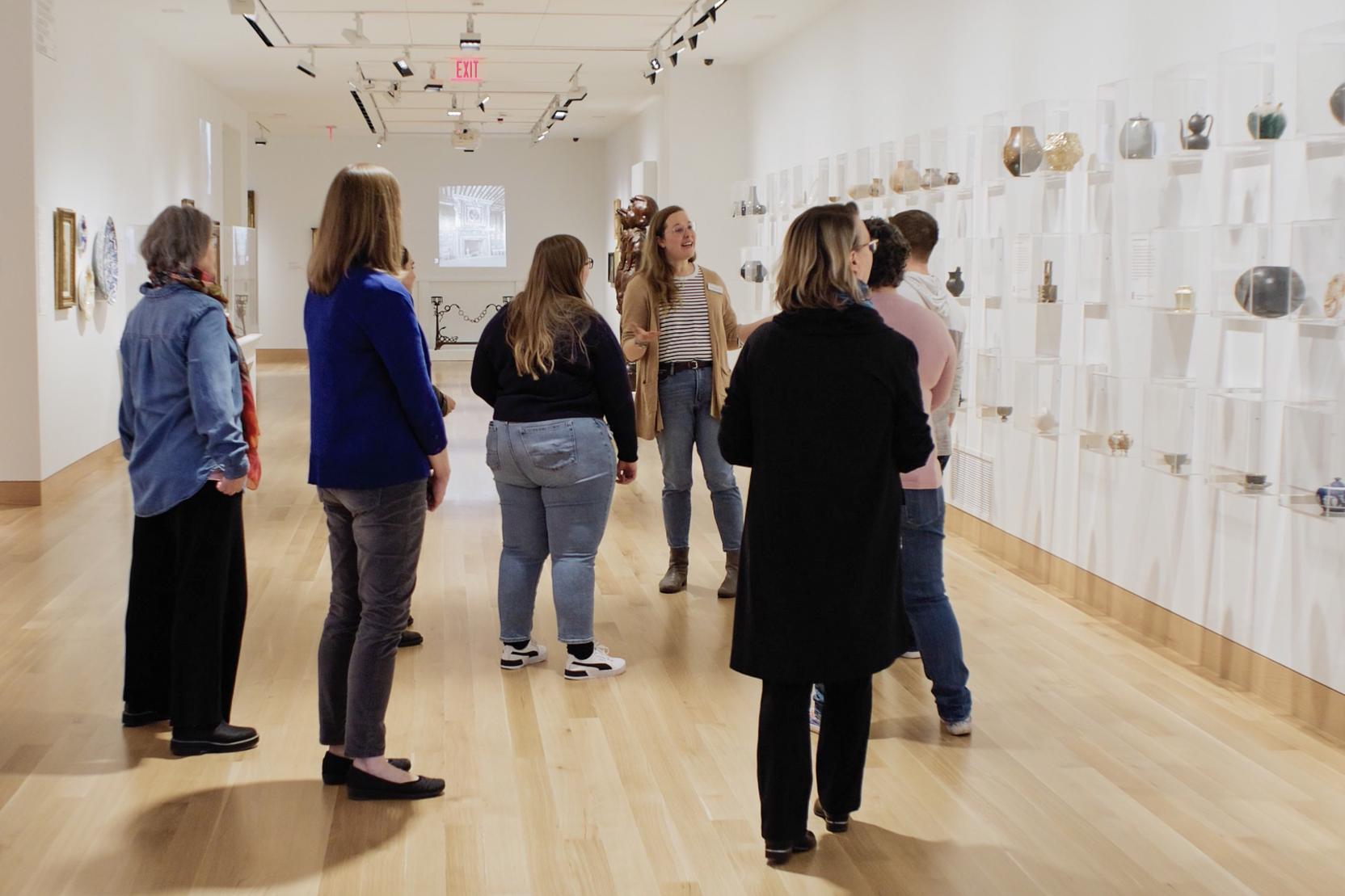 A woman with long brown hair leads a group of adults on a tour in a museum gallery