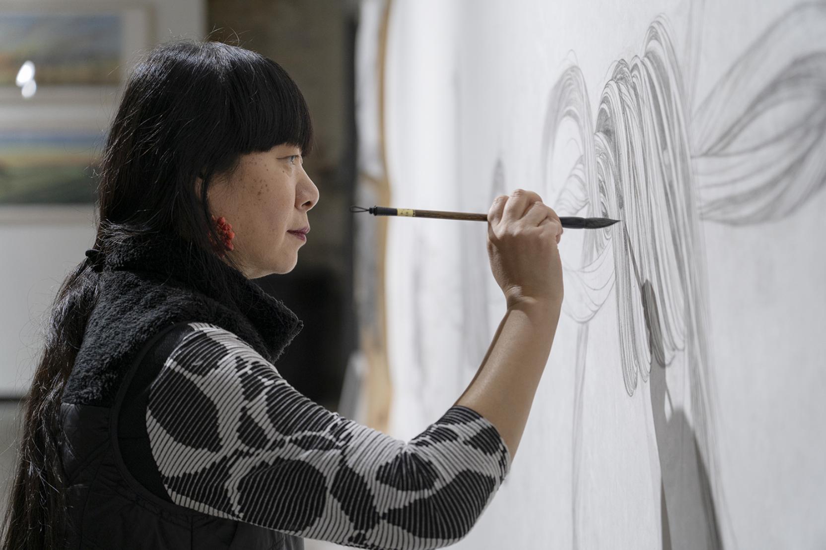  A woman paints a large white canvas with black ink