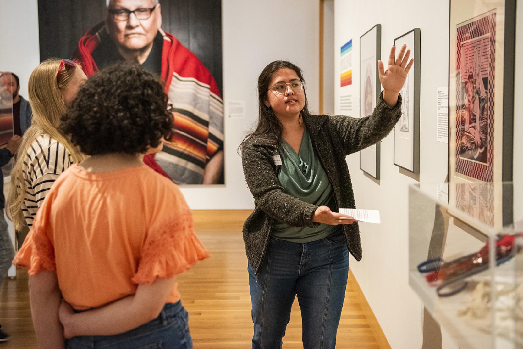 A woman gestures to a work of art while two other people look on