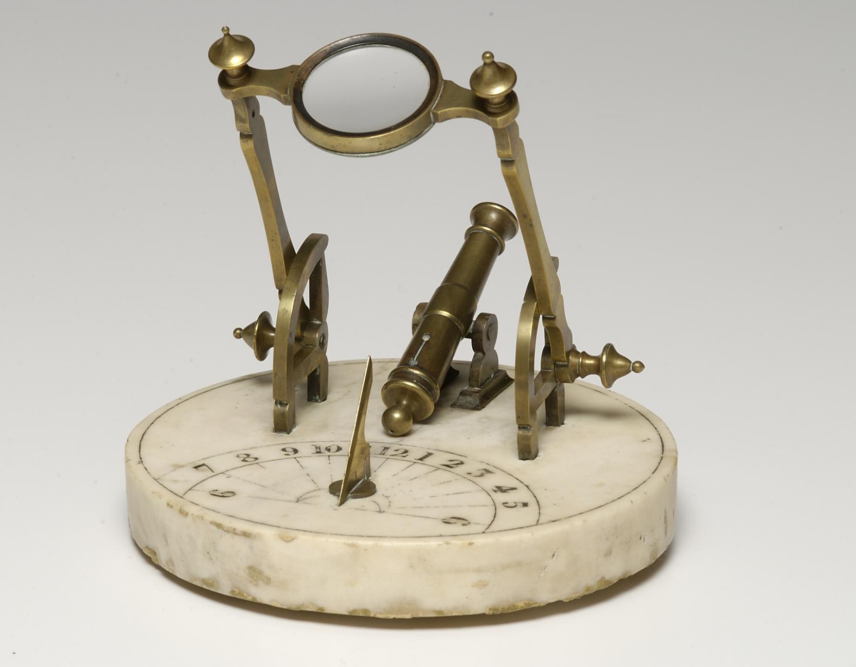 A decorative brass cannon and looking glass are attached on top of a circular marble slab etched with golden numbers