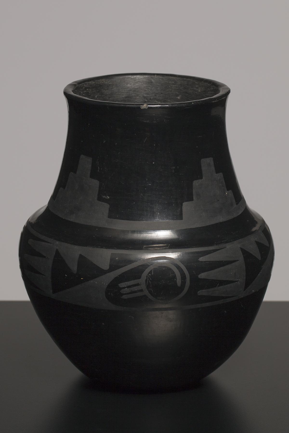 A shiny black jar with a globular body and long neck, decorated with a matte black geometric pattern