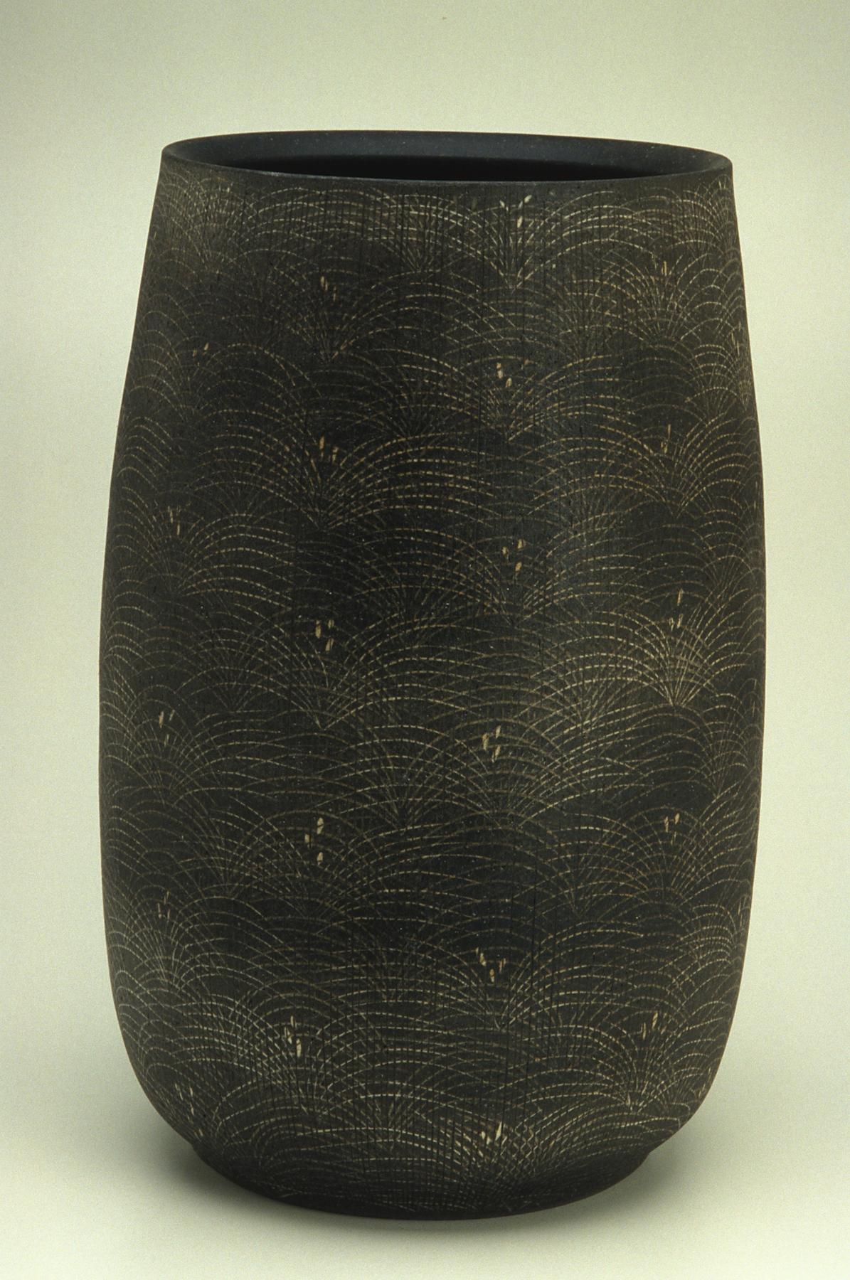 Cylindrical charcoal-colored vase with a repeated light gray design of layered arches and dot clusters, overlaid with incised vertical lines