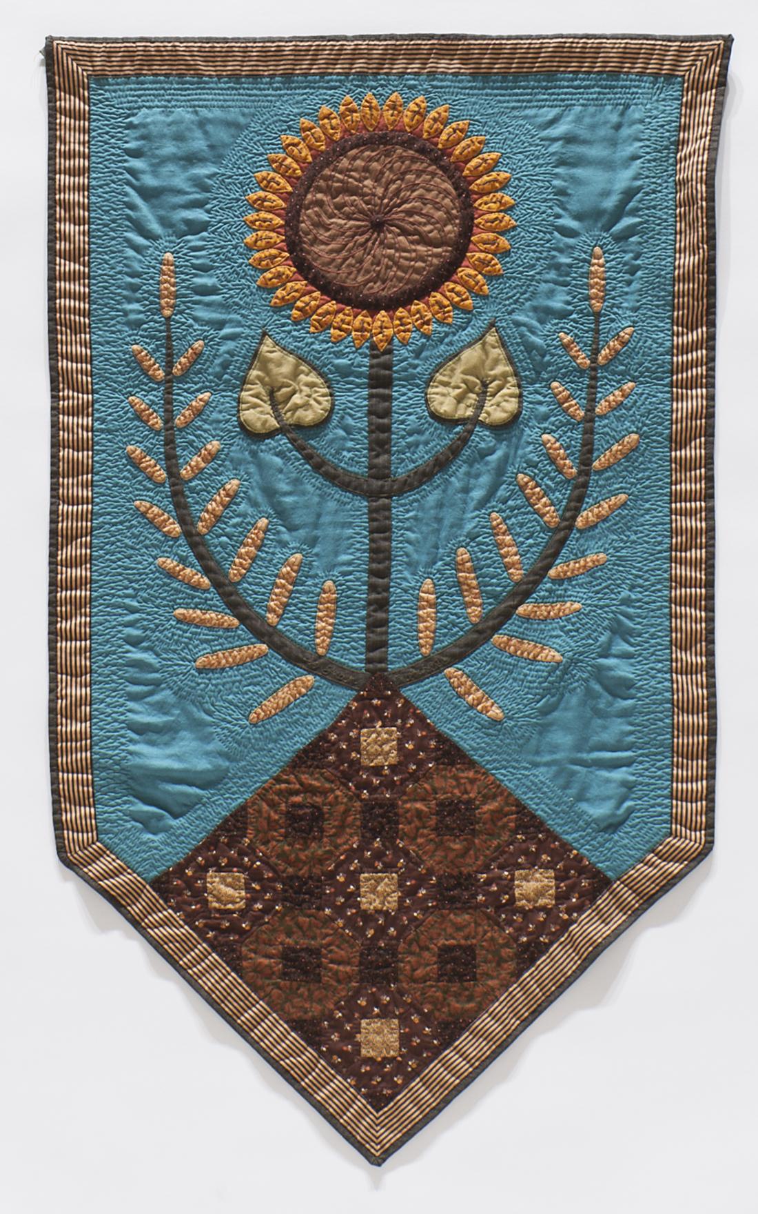 A blue quilted banner featuring a sunflower planted in dirt encircled by stalks of wheat 