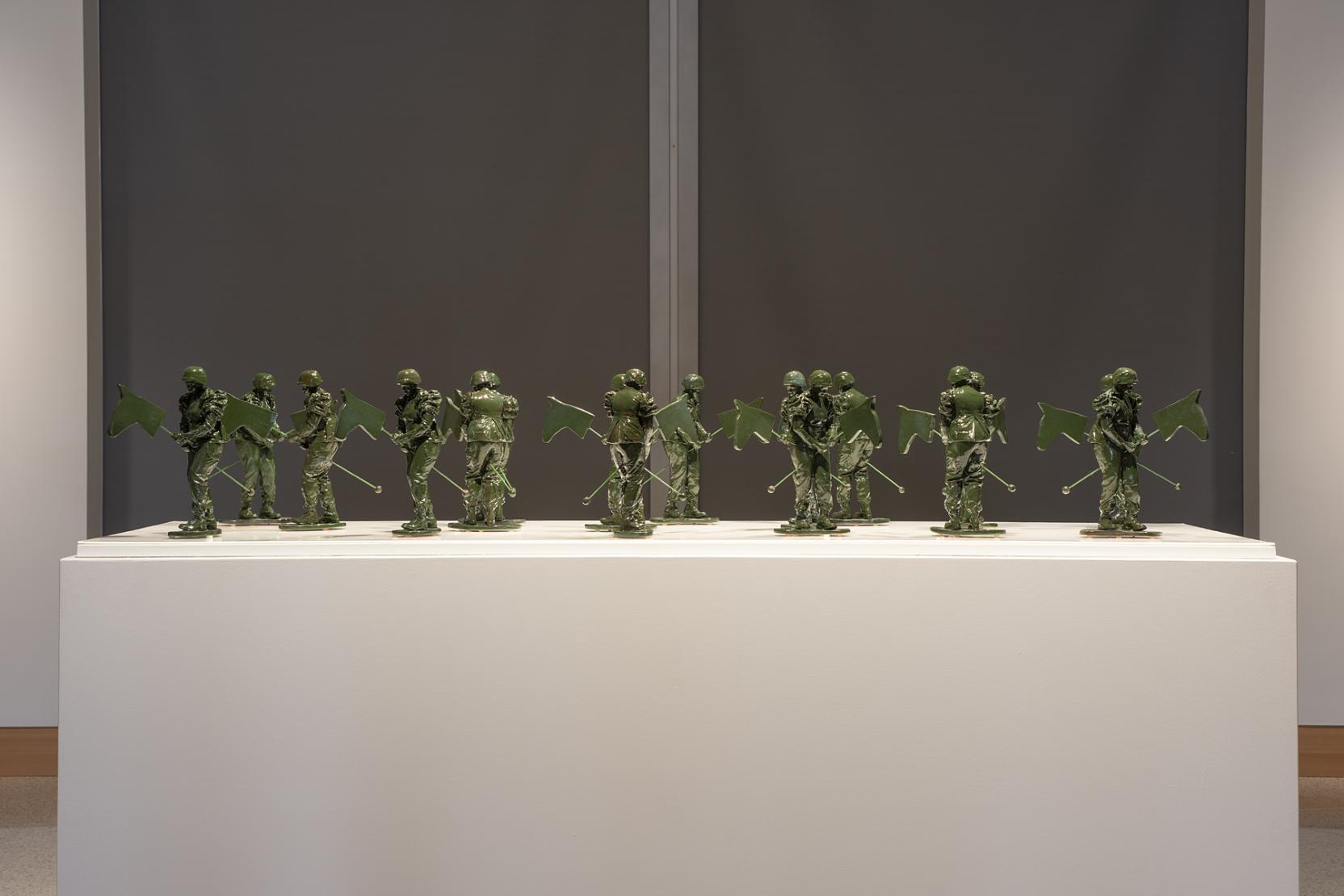 16 small green solider figurines on top of a white pedestal 