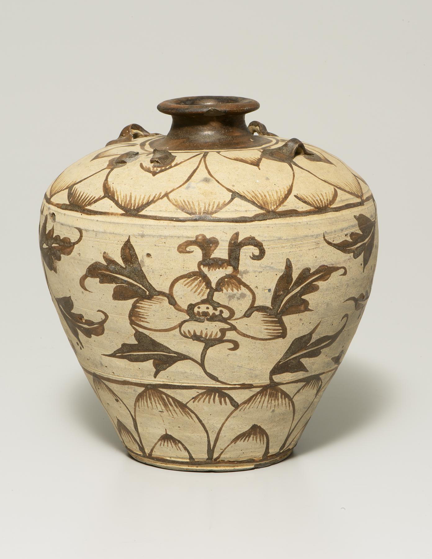 A tan jar that is narrow at the bottom with a wide shoulder and narrow mouth is decorated in brown with a petal design at the top and bottom and flowers in the middle
