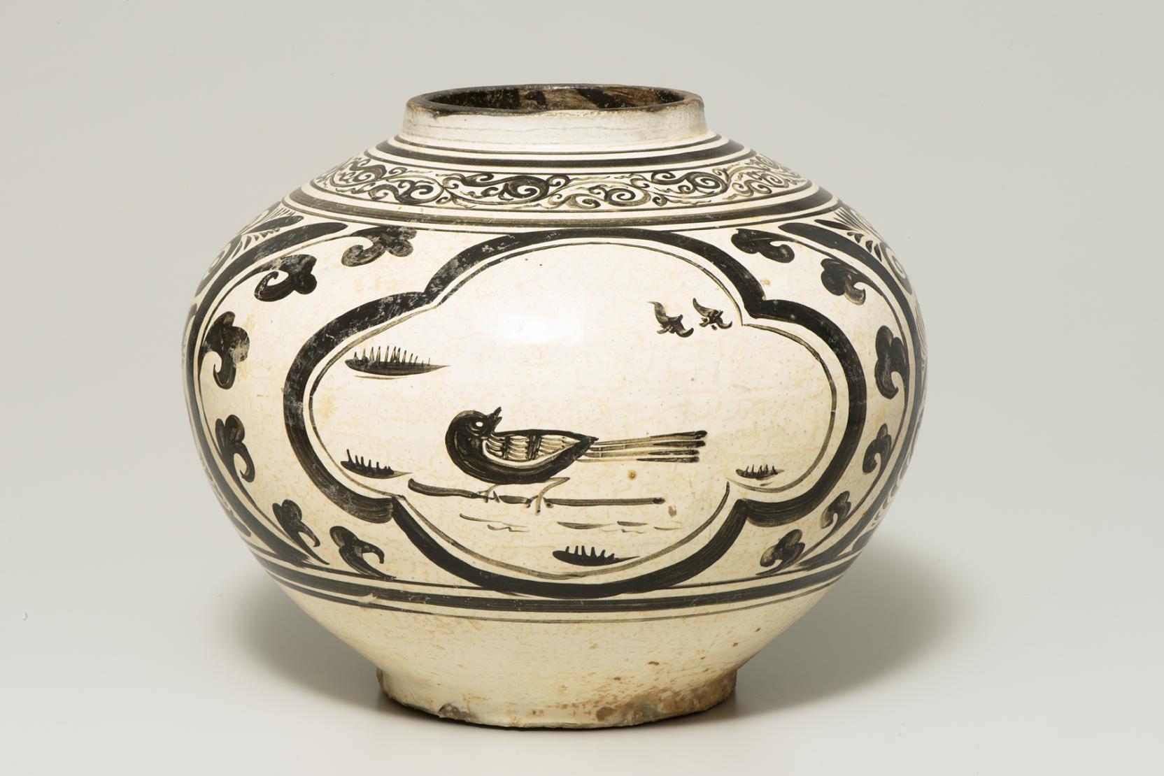 A round, cream-colored jar decorated with a single black bird and other swirling black designs