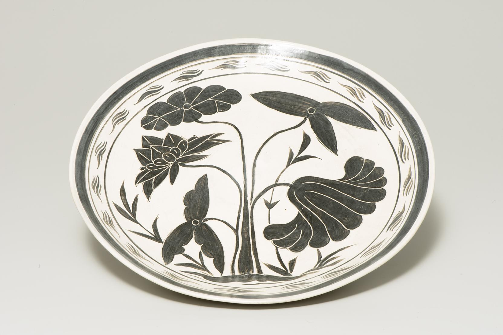 white plate with five stemmed black flowers at center and a ribbon of black around the edge 