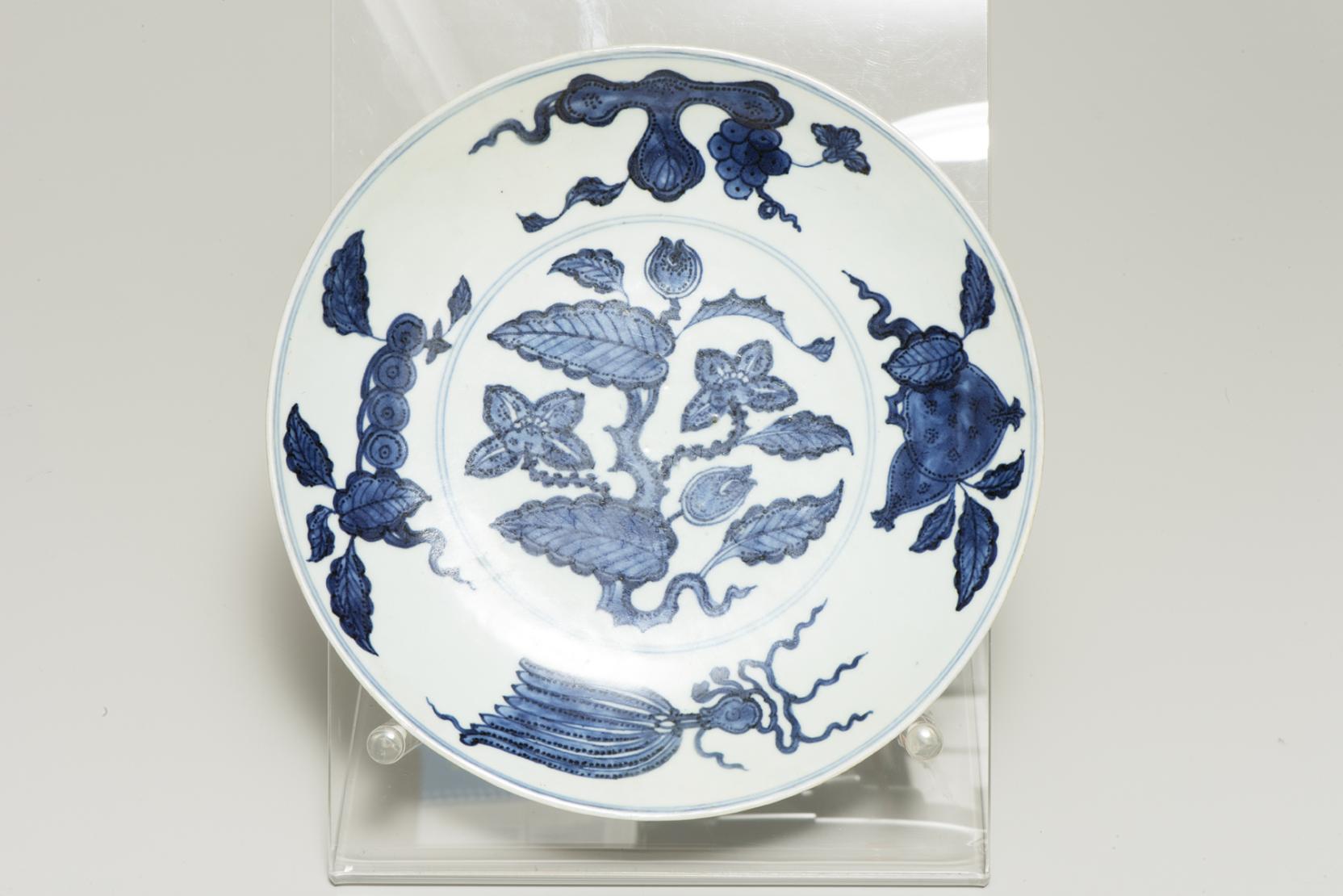white plate decorated with blue flowers at center and a dark blue grape and pomegranate around the wide edge