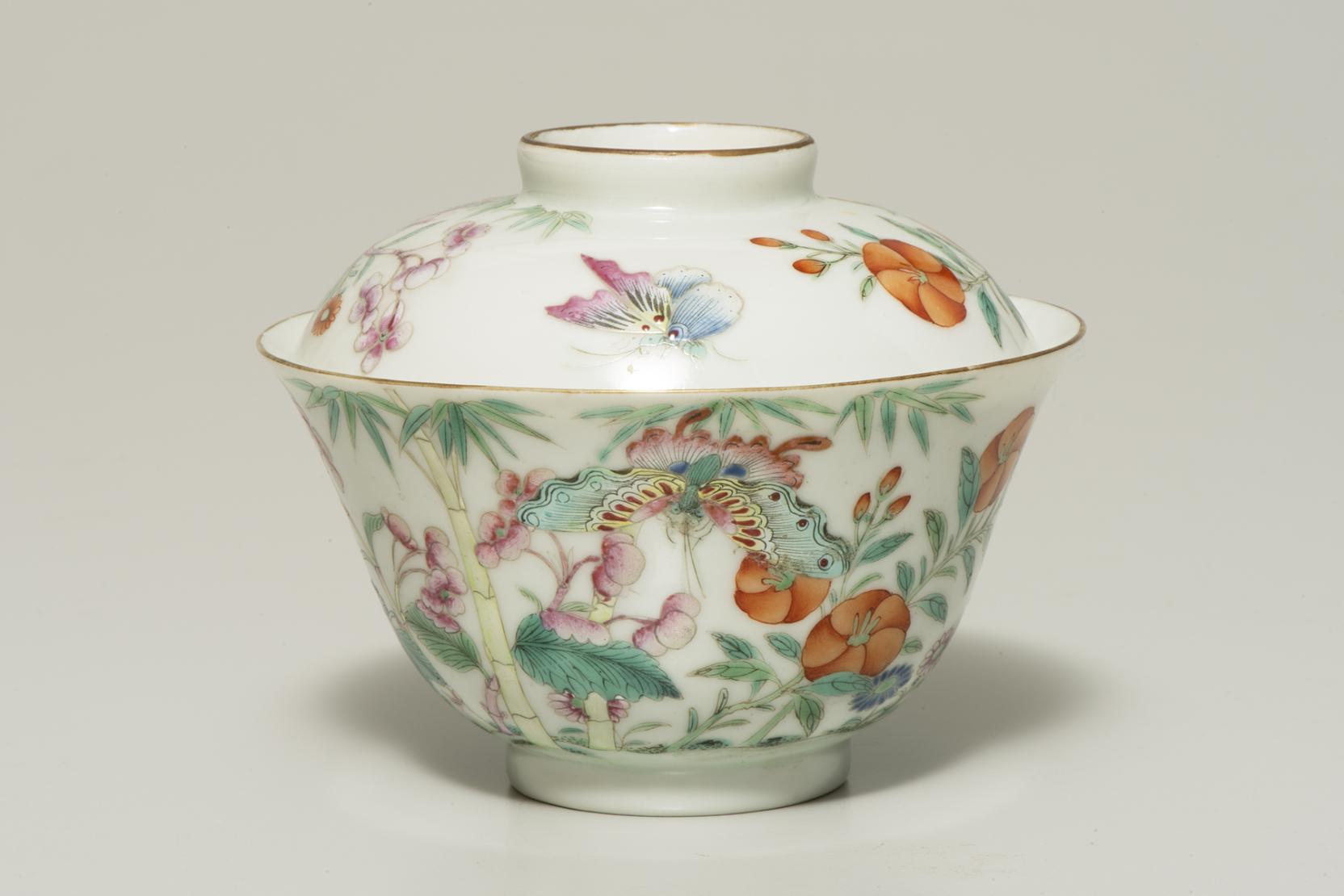 A white lidded bowl decorated with pink and green butterflies, green leaves, and round orange flowers