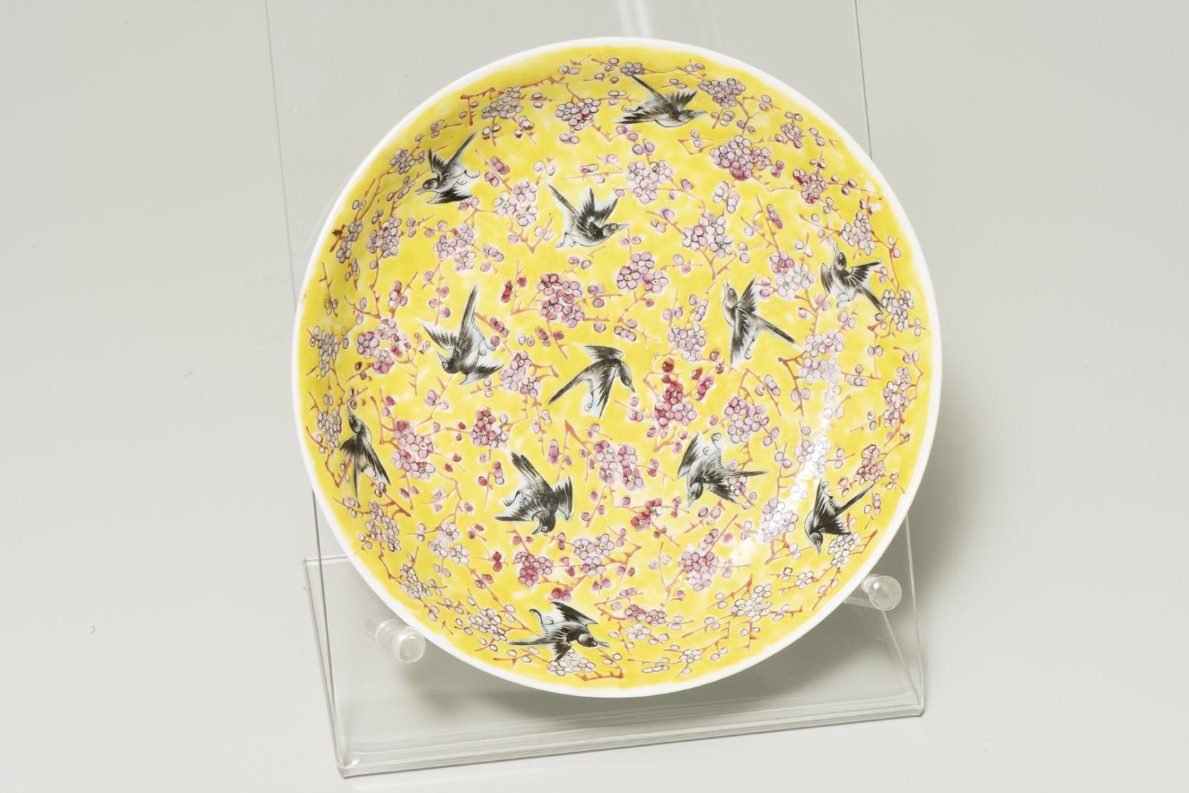 yellow plate with a dozen brown birds flying amidst pink-blossomed branches