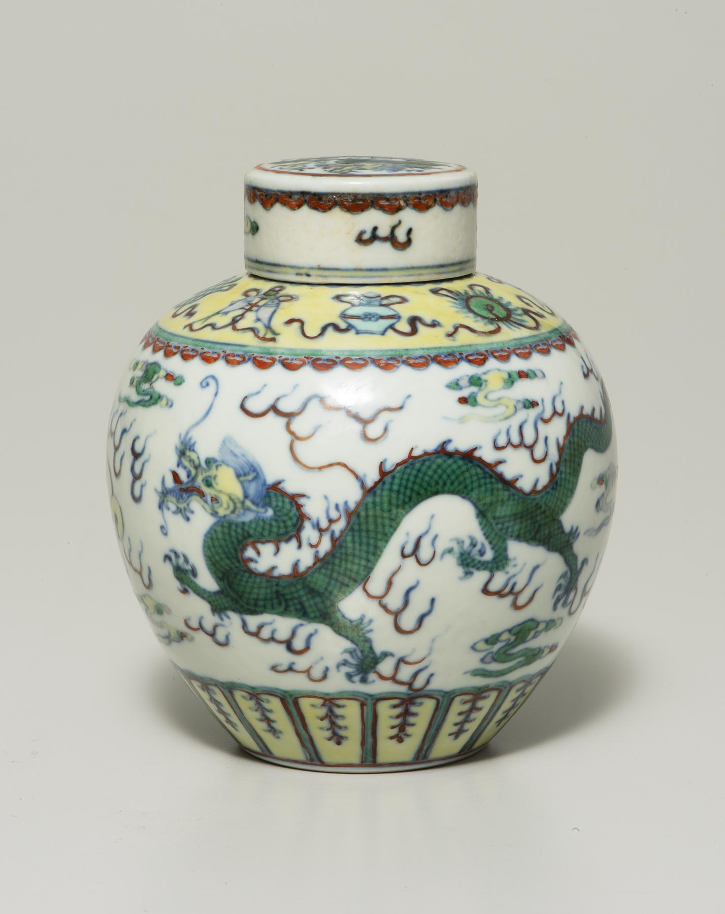 a green dragon winds around a white lidded jar that has a pale yellow rim and base decorated with red, blue and green