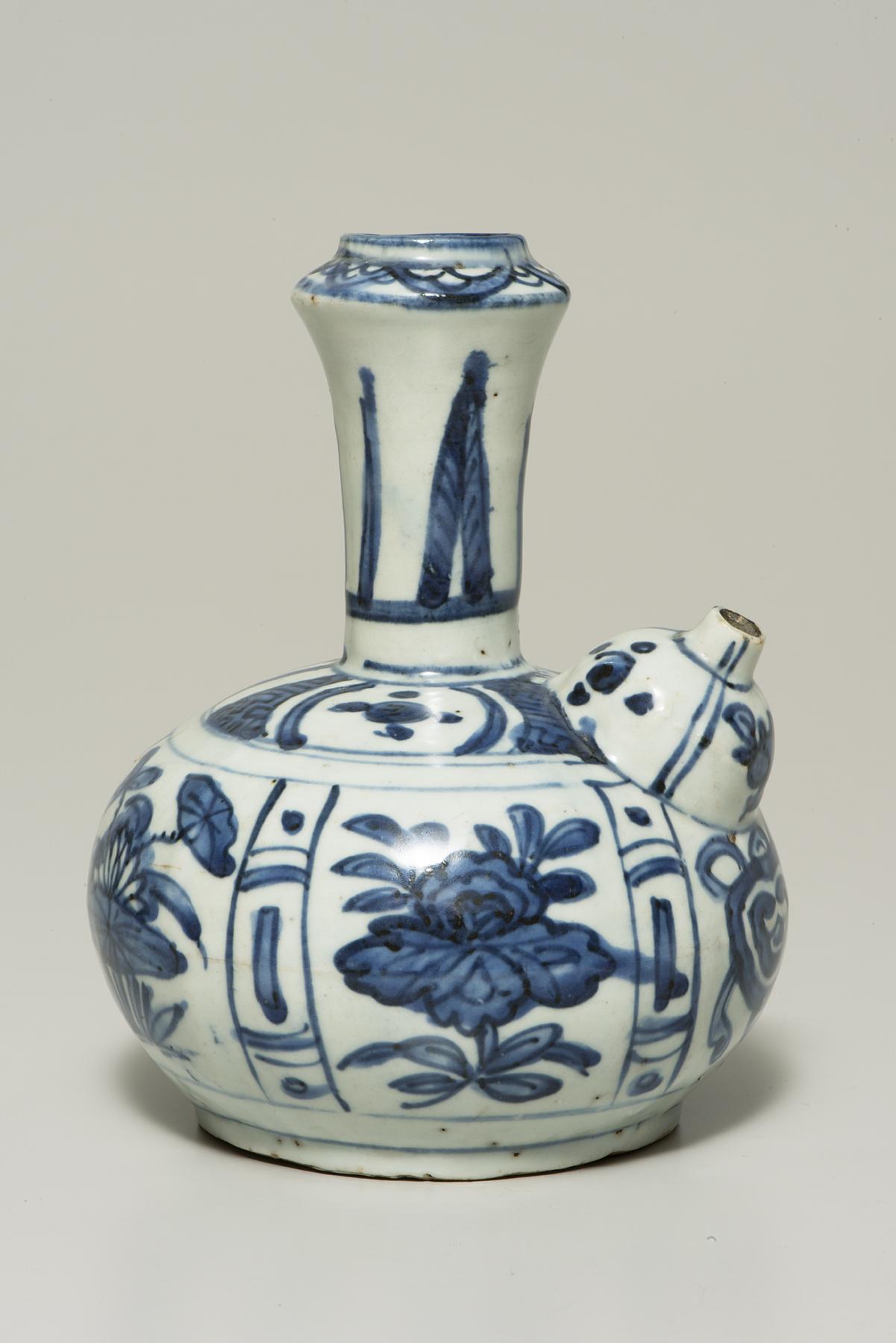 White pitcher decorated with blue floral designs and other patterns has a tall central spout and a smaller one on the right
