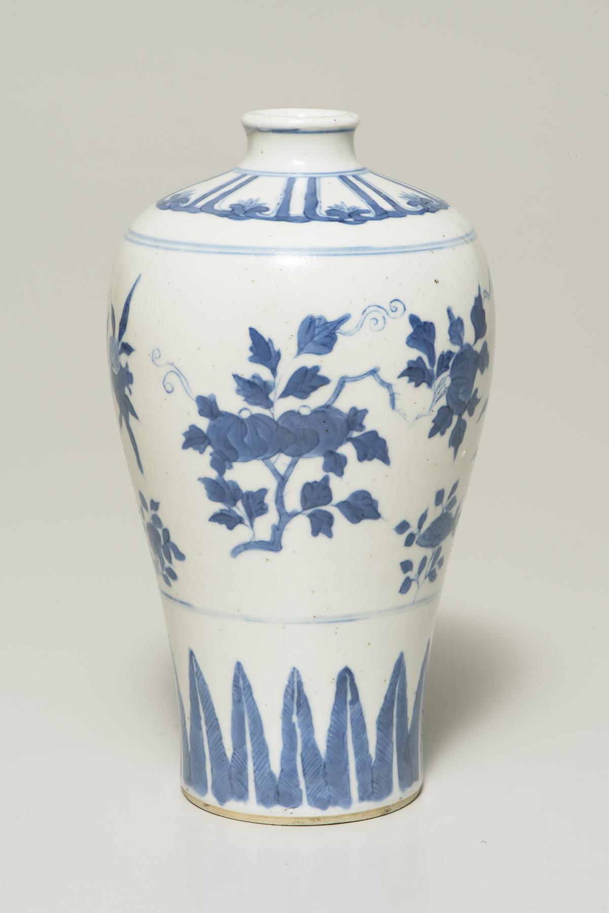 A tall white vase with a narrow mouth decorated in blue with a variety of fruit trees