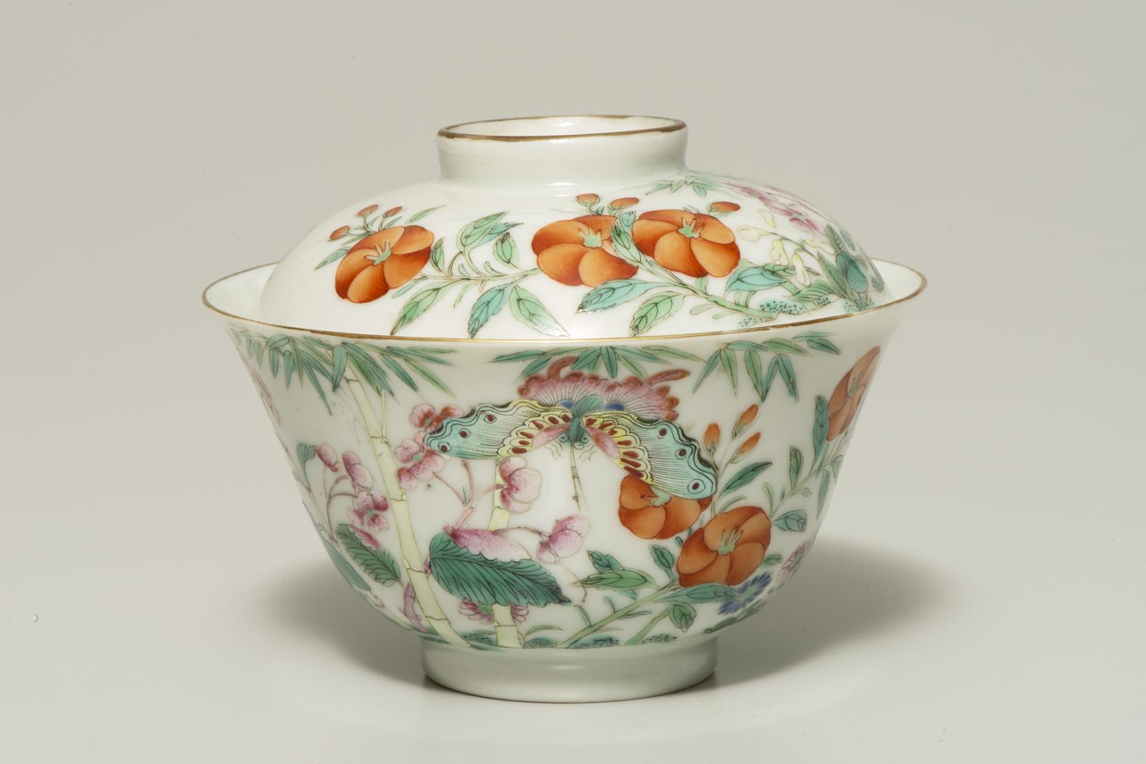 A white lidded bowl decorated with pink and green butterflies, green leaves, and round orange flowers