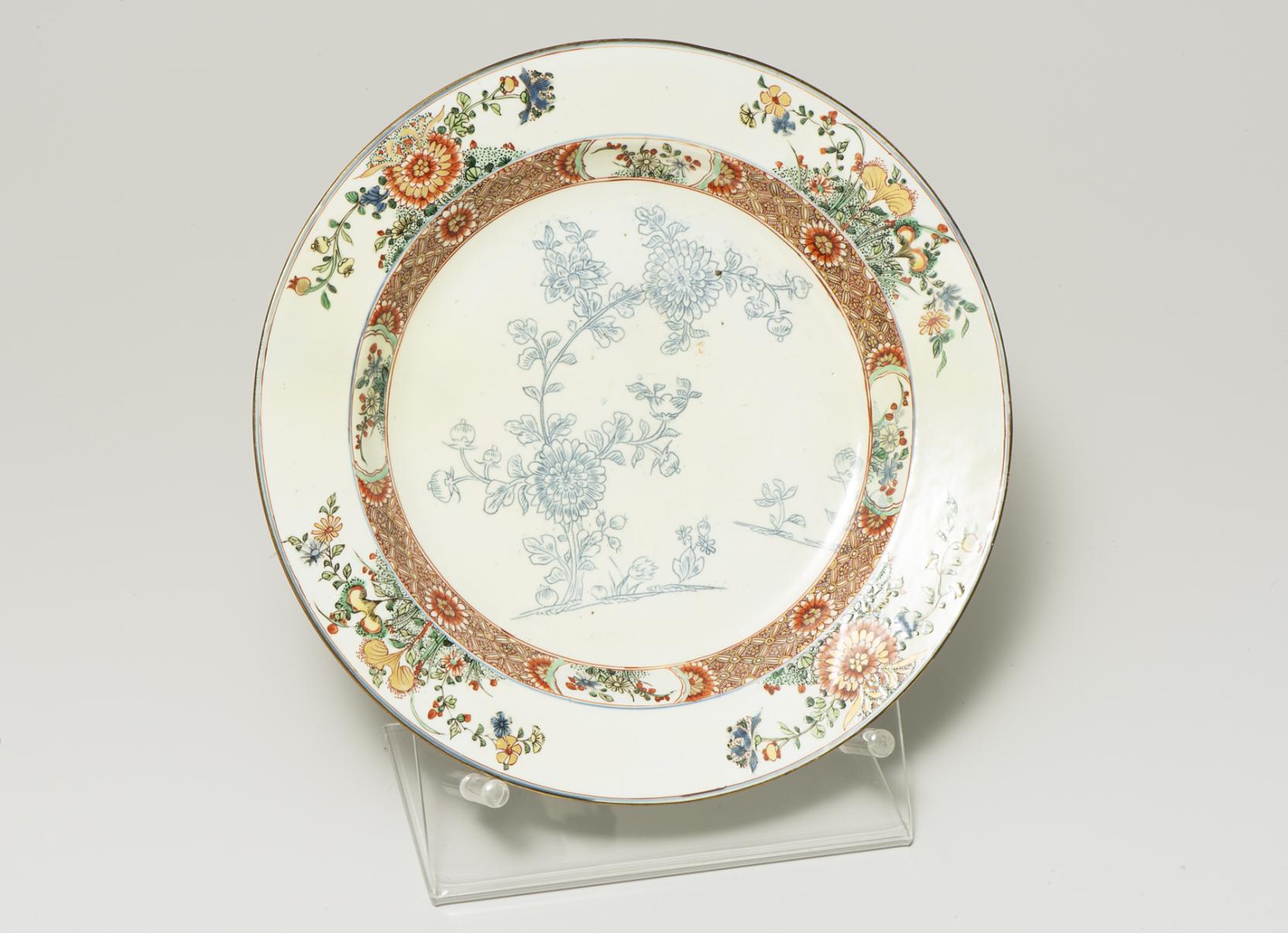white plate decorated with a delicate blue floral design at center bordered by a band of dense brown texture and four bouquets of orange flowers 