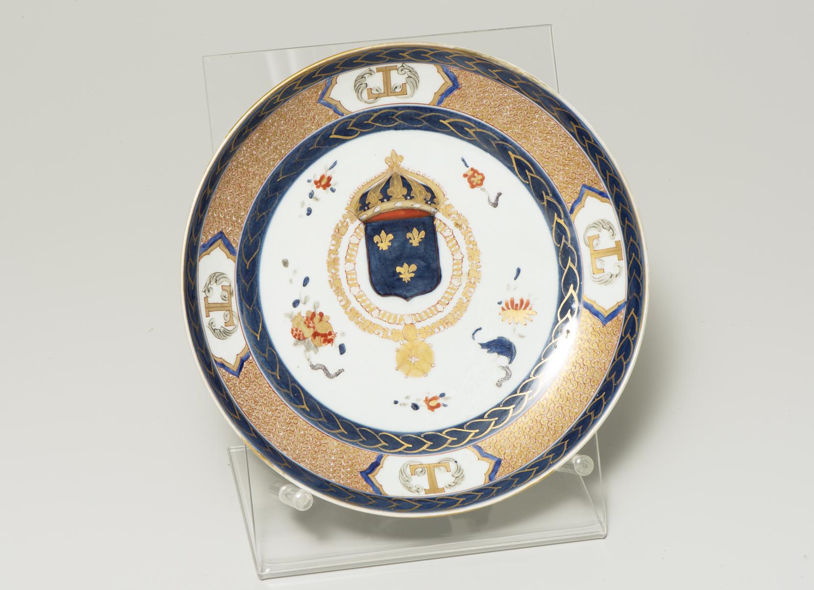 white plate with a navy blue coat-of-arms with gold fleur-de-lis at center bordered by dense orange texture surrounded by navy and gold