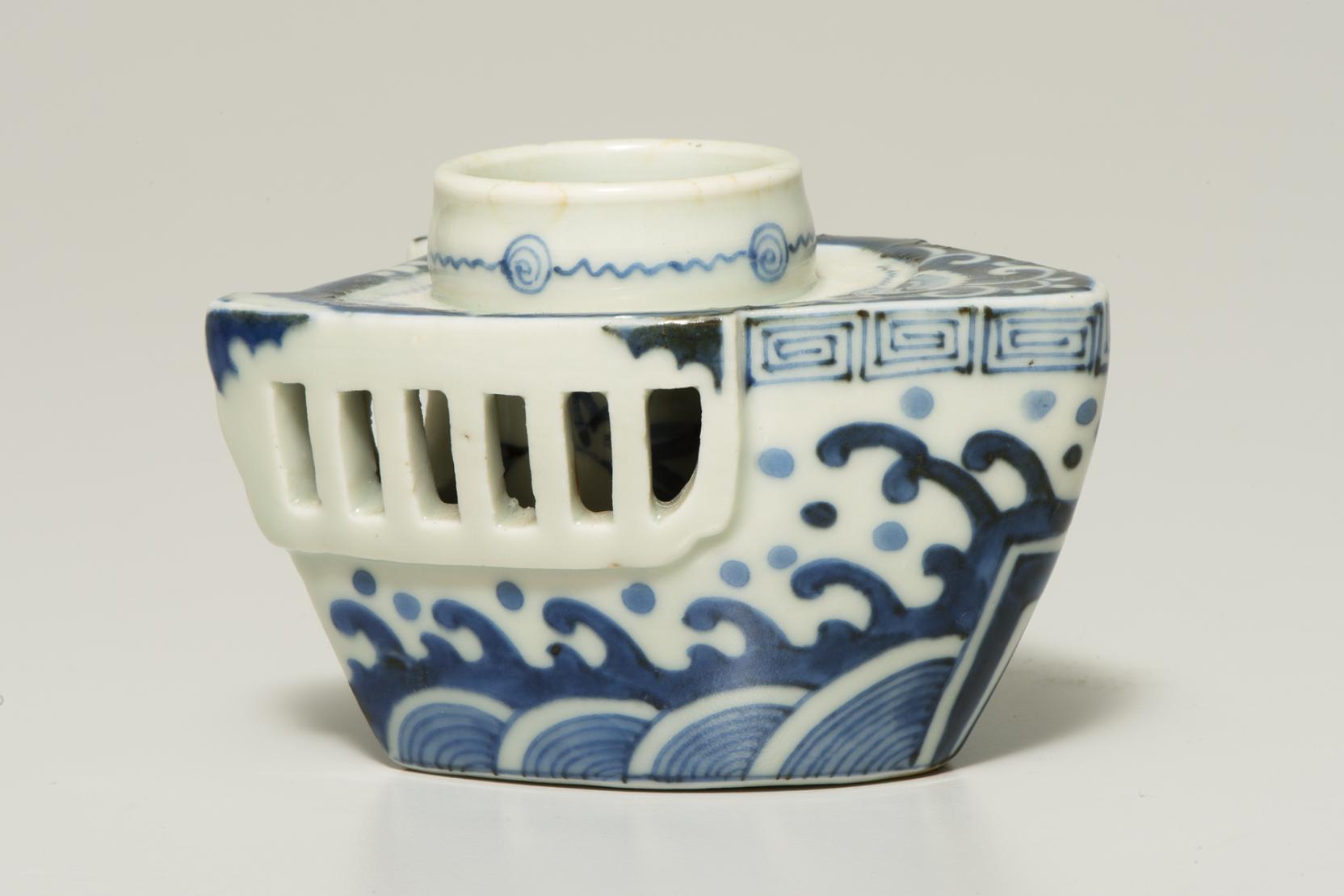 a small, white candlestick shaped like a boat is decorated with blue waves and geometric patterns