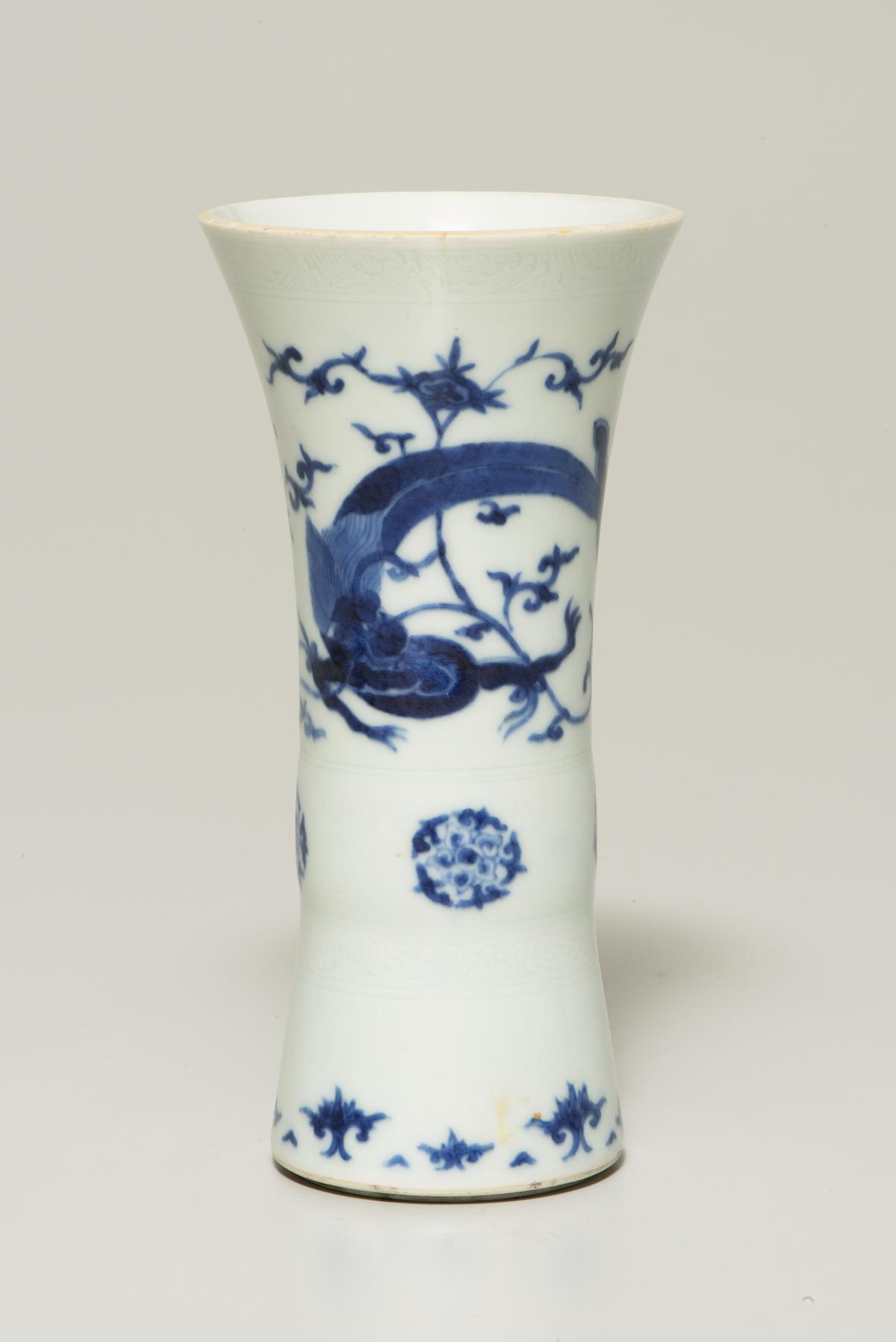 A slender white vase that flares at the top decorated with a blue dragon and floral designs