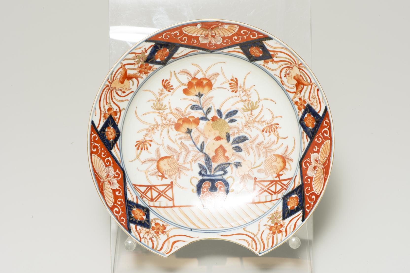 white plate with a semicircular cutout at the bottom of the rim decorated with a vase of orange flowers and three moths equally placed around the border