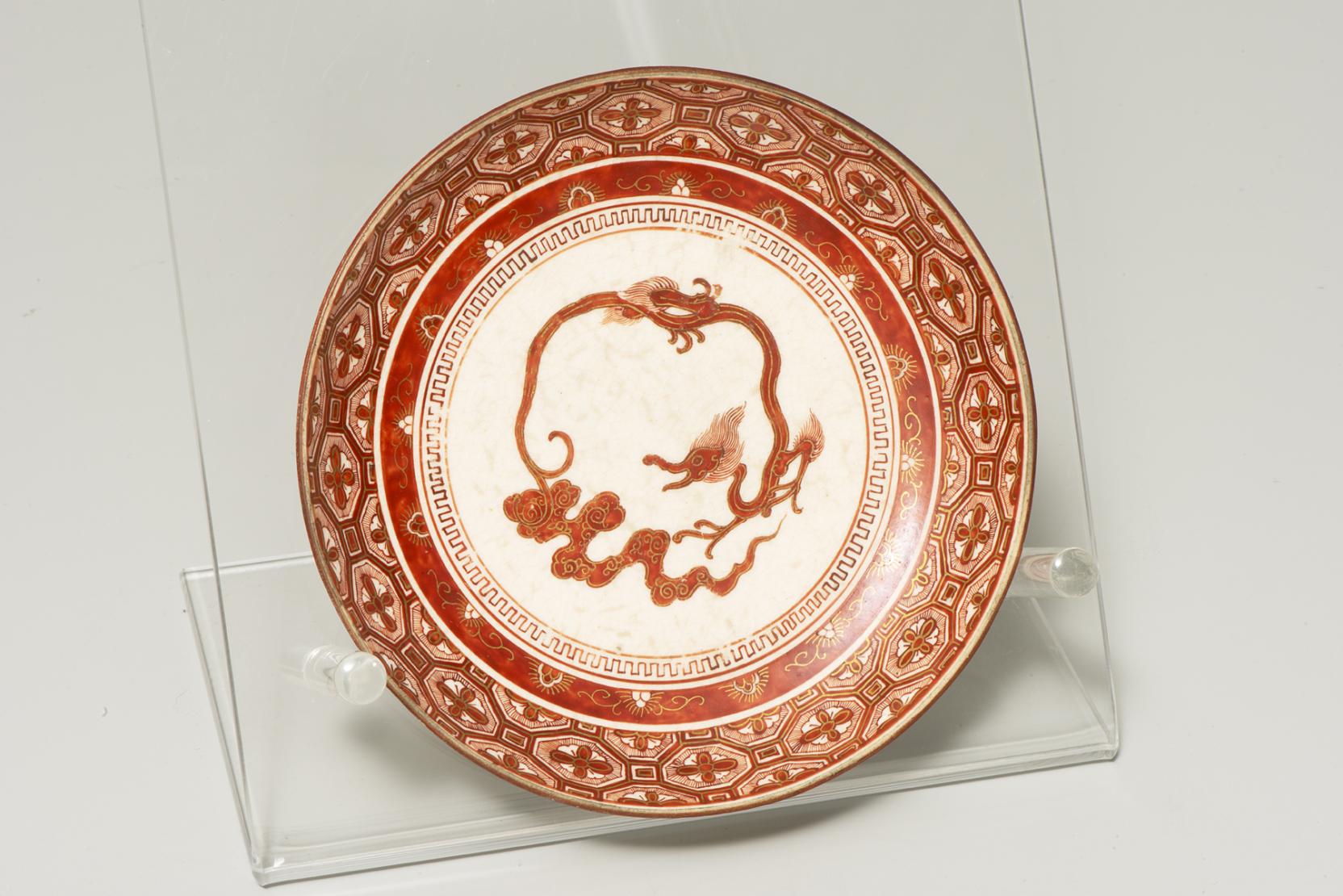 white plate decorated with a red-orange serpentine dragon at center and dense red-orange textures around the border