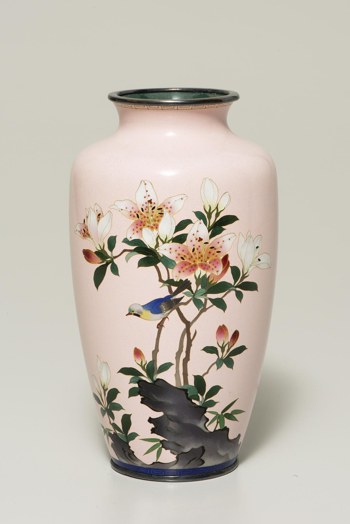 A tall pink vase decorated with blooming white and pink lilies and a blue bird with a yellow throat