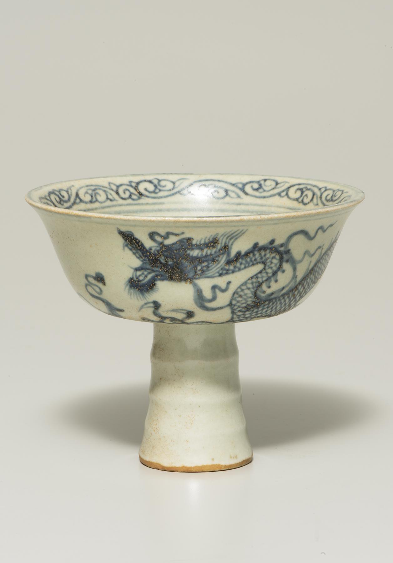 A white cup decorated with a blue dragon stands on a narrow white stem 