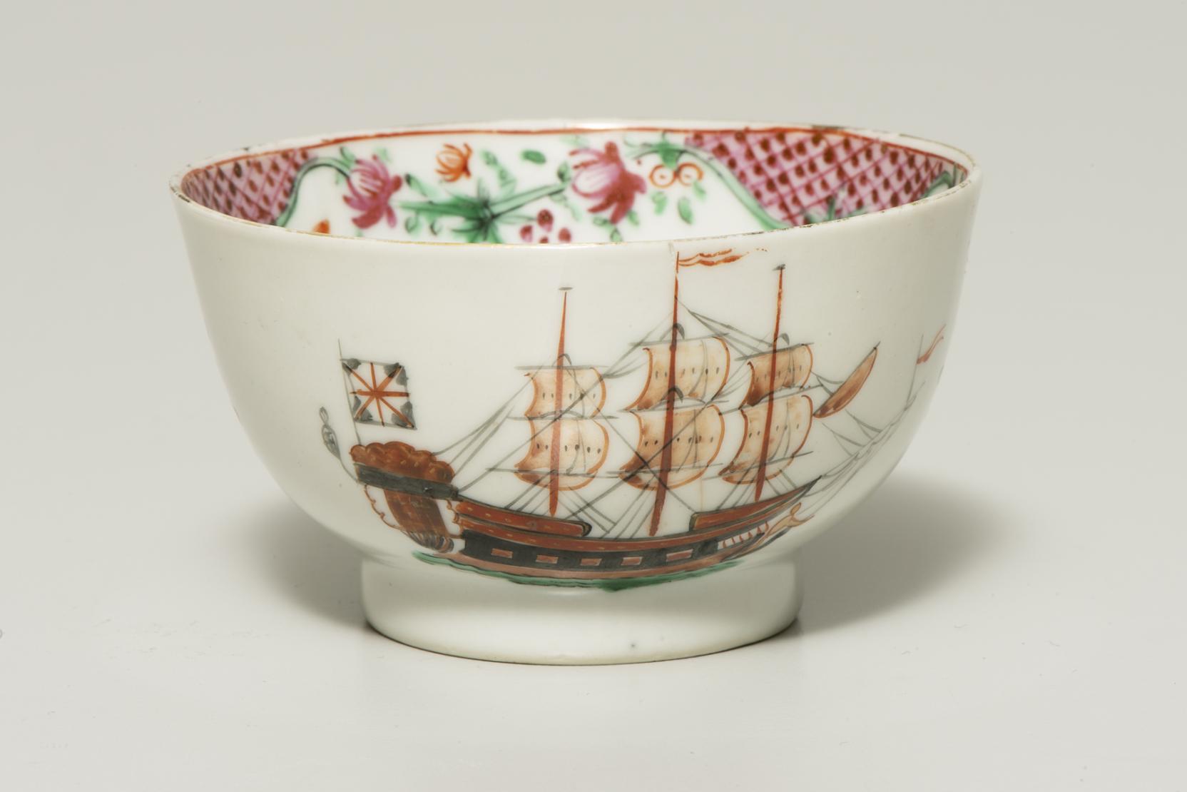 a white bowl decorated with a three-masted sailing ship flying a version of the Union Jack; what is visible of the interior is decorated with a red geometric pattern and red flowers  