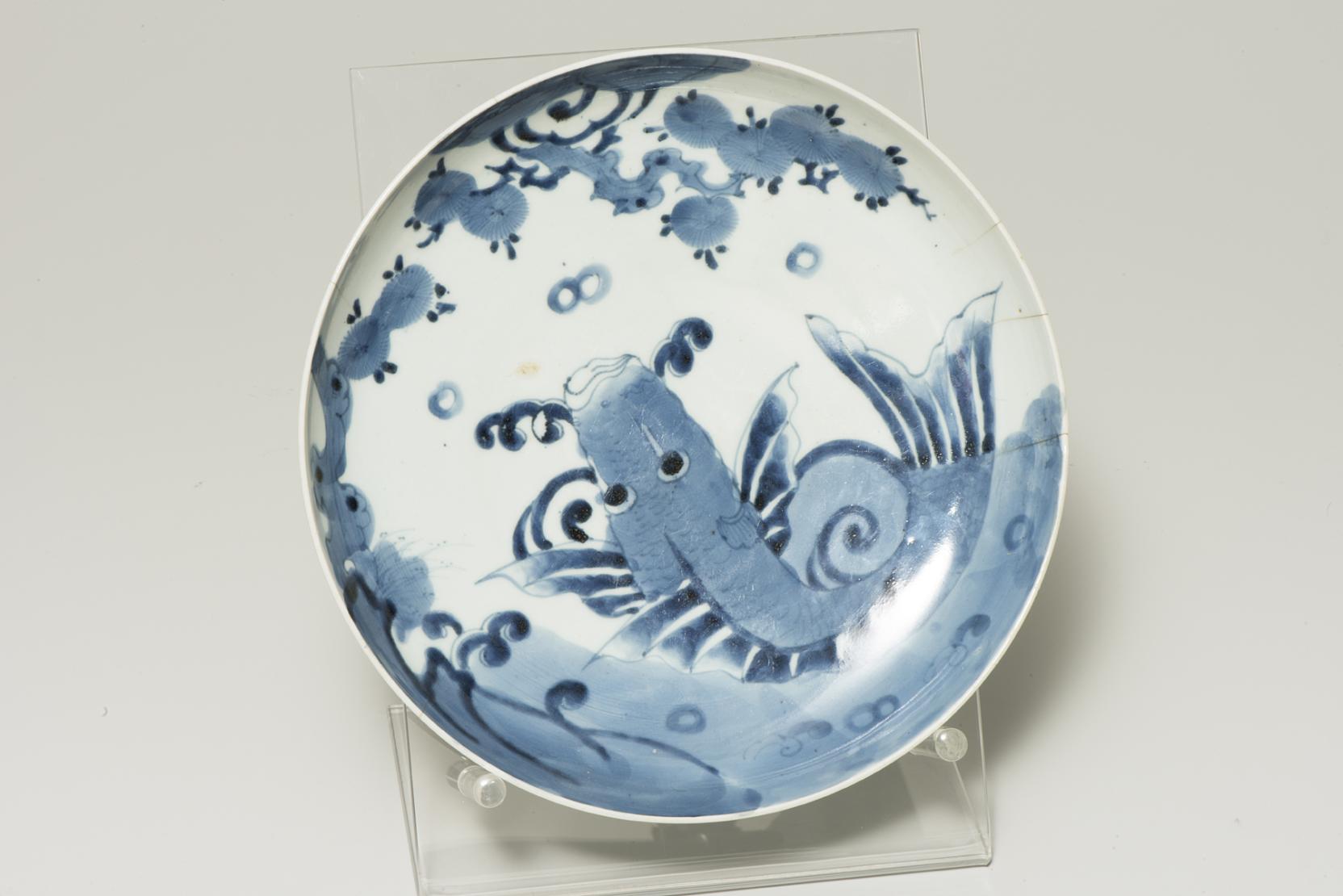 white plate with a blue koi fish jumping out of the water toward blue tree branches