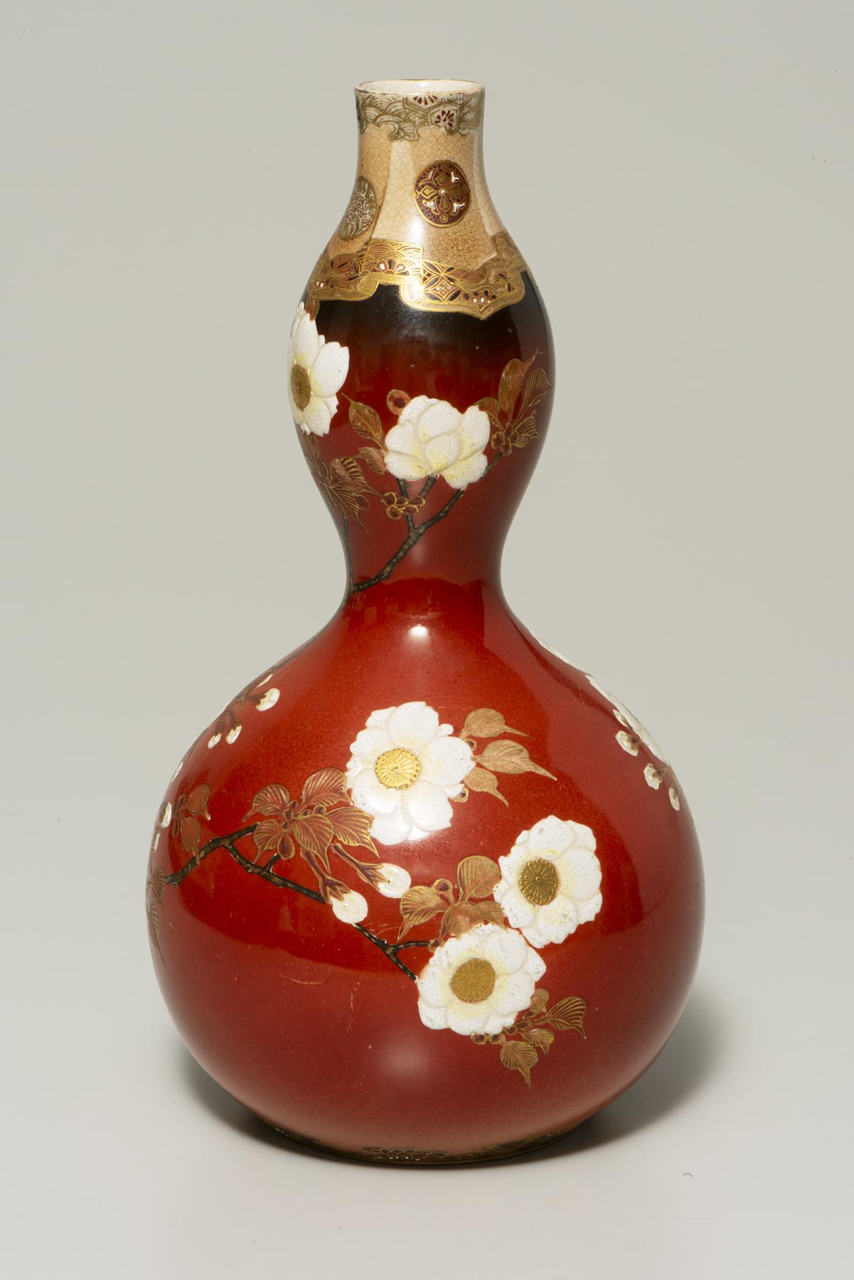 A red, gourd-shaped bottle decorated with branches and white flowers with a yellow center