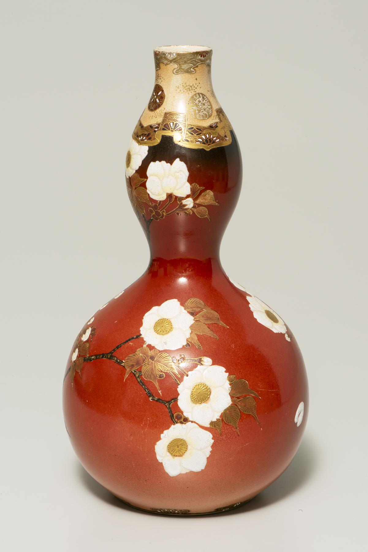 A red, gourd-shaped bottle decorated with branches and white flowers with a yellow center